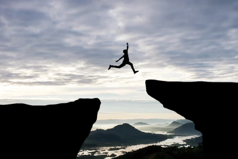 Man jump through the gap between hill.man jumping over cliff on sunset background